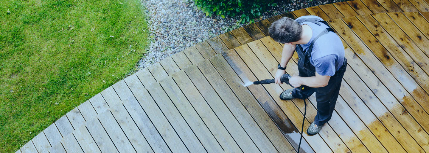 man pressure washing a wooden deck flooring
